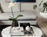 En vit orkidé i en mörk vas, böcker och en svart ask med blå sten utgör en elegant dekoration soffbord.