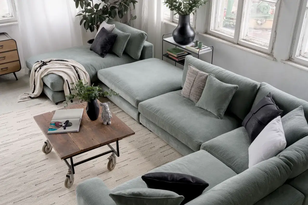 Stor, ljusgrön modulsoffa med många kuddar. En mysig soffa inspo med en träbricka som soffbord.