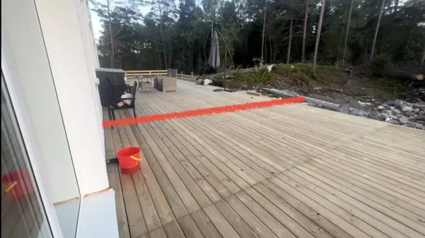 Nybyggd altan med en röd markering som visar var ett vindskydd ska byggas. Trädgårdsmöbler och en parasoll finns på plats.